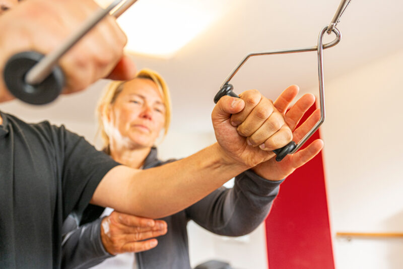 Symbolfoto einer Person, die unter Aufsicht an einem Seilzuggerät trainiert